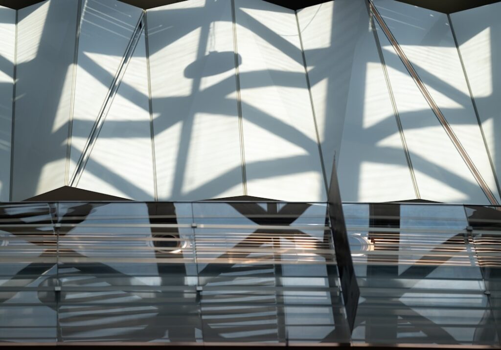 Geometric shadows fall across a white pleated architectural surface.