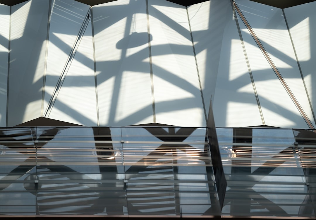 Geometric shadows fall across a white pleated architectural surface.